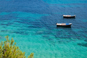 Two boats at rest in shallow water. Crystal clear turquoise waters of the Adriatic sea. Eastern bank of the famous Zlatni Rat (Golden Horn) beach in Bol on Brac island, Dalmatia, Croatia.