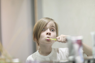 School-age boy with a stylish haircut brushes his teeth in front of a mirror in the dentist's office
