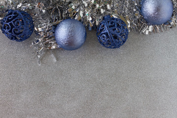 Christmas Frame Decoration. Blue shiny balls and a metallic silver tinsel. Silver metallic glitter background. Copy Space