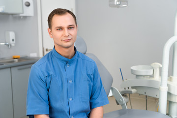 confident young dentist sitting in dentist office and looking at camera