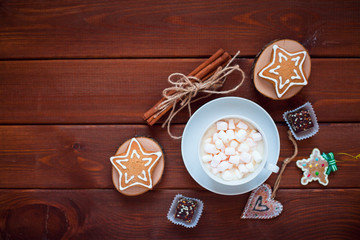 Cup of chocolate with marshmallow, gingerbread cookies, gifts and beautiful Christmas decorations on the wooden background. Flat lay, top view, space for a text.