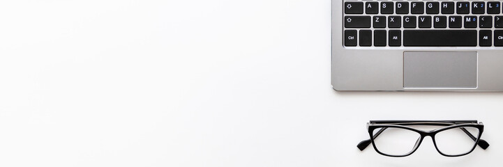 Panoramic photo of white desk copy space seen from above with a laptop keyboard and black glasses