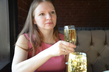 beautiful blonde girl holding a glass of champagne or wine, drinking champagne in a restaurant, in an evening pink dress, on a date or meeting