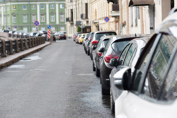 A number of cars parked in a continuous stream to the right side of the road. The bustle of the...