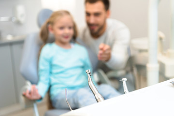 close-up shot of dentist tools on stand with blurred father and daughter on background