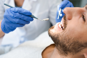 cropped shot of dentist examining teeth of handsome smiling client