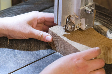 Craftswoman is cutting a wood workpiece from wood with bandsaw. Close-up hands.