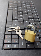 Golden locked padlock and keys on black computer laptop or tablet keyboard. Concept of internet password security, data privacy, cybercrime prevention. Selective focus.