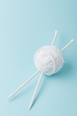 close up view of white yarn ball and knitting needles on blue background