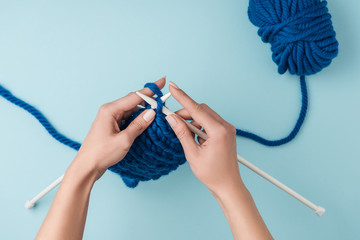 cropped shot of woman knitting on blue background with blue yarn