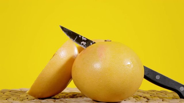 A bunch of pomelo fruits (exotic variety of the Citrus familiy), full and halved, with a knife, on a rotating surface. Medium close-up shot.