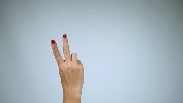 Woman raising two fingers up  and showing peace or victory symbol or letter V. Female one hand holding two fingers up in sign language on light background. Fingernails with fresh red glossy manicure.