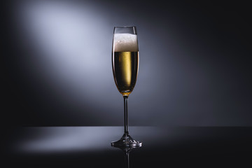close up view of glass of champagne with foam on dark backdrop