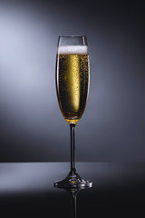 close up view of glass of champagne with foam on dark backdrop