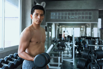 Naklejka premium Young asian man lifting dumbbells in gym. healthy lifestyle and workout motivation concept.