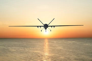 Foto op Plexiglas Unmanned military drone patrols the territory at sunset, flying above water surface. The view is straight ahead. © aapsky