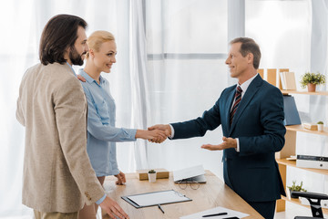 smiling woman and insurance agent shaking hands in office