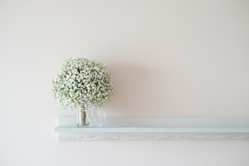 Bridal bouquet of gypsophila on a white wooden shelf against a light wall - selective focus, copy space