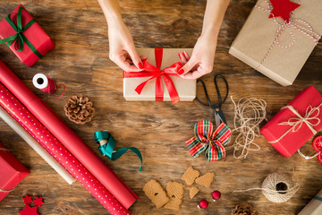 DIY Gift Wrapping. Woman wrapping beautiful christmas gifts on rustic wooden table. Overhead view...
