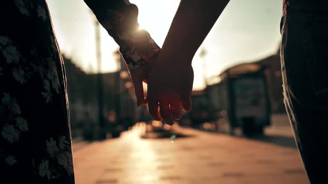 Couple hands holding each other on city street sunset light with beautiful lens flare. Male and female lovers touching their arms. Super slow motion shot.
