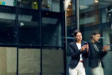 Businesswoman using mobile phone, standing near office building