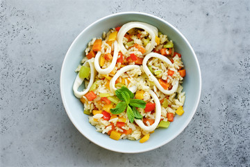 Rice with vegetables and squid rings. Top view, gray concrete background