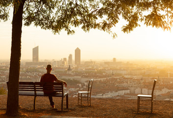 Man on a bench enjoying the summer sunrise over a city. Lyon, France.