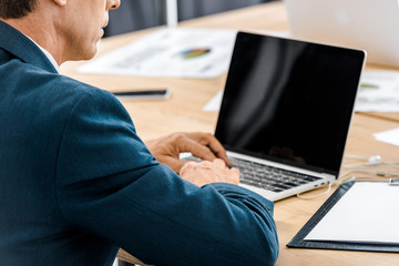 Adult businessman using laptop with blank screen in office