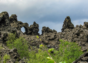 Fototapeta premium Dramatic black lava rock structures, unique volcanic flow formations and green Icelandic forest, Myvatn area, Northern Iceland, Europe.