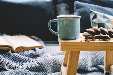 Cup of hot drink on wooden table. Living room interior with blue sofa on background. Cozy winter or autumn concept