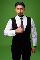 Young bearded Iranian businessman against green background