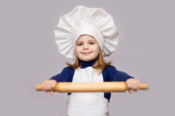 Children cook. Happy little girl in chef uniform holds rolling pin isolated on white background