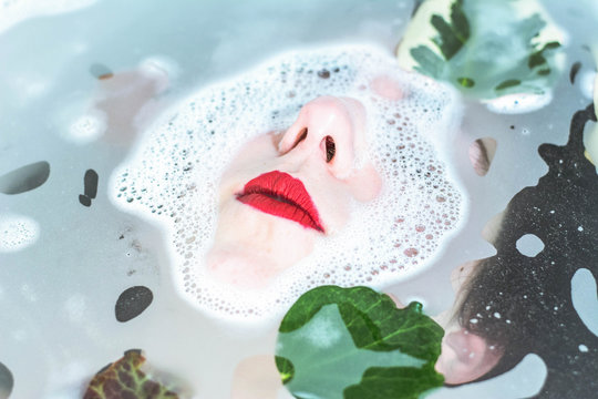 Woman with red lips in water with leaves