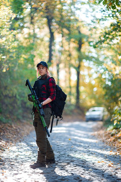 Woman with rifle in the forest. Car in the background/Red-haired young woman with a rifle on the road in the forest. Car in the background