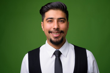 Young bearded Iranian businessman against green background