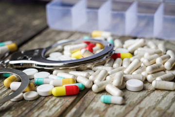 Handcuffs and pills and drugs on wooden table.