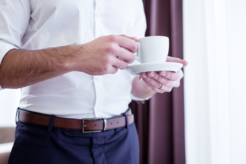Freshly made coffee. Close up of a cup with coffee being in hands of a handsome smart successful entrepreneur