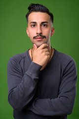 Young handsome Iranian man with mustache against green backgroun