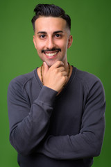Young handsome Iranian man with mustache against green backgroun