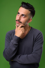 Young handsome Iranian man with mustache against green backgroun