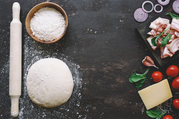 Raw yeast dough  and essential ingredients for pizza. Dark food background. Copy space for text