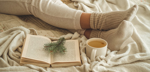 Fototapeta na wymiar Cozy winter evening , warm woolen socks. Woman is lying feet up on white shaggy blanket and reading book. Cozy leisure scene