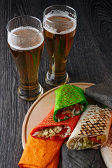 Beer in a glass and shawarma in pita bread is cut and lies on a wooden surface. The Middle Eastern dish is prepared on the grill and served with sauce.