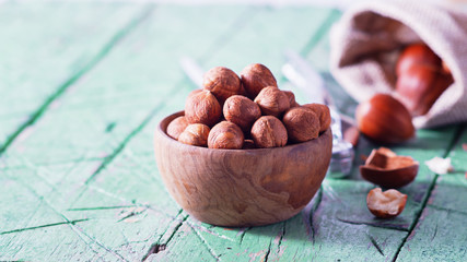 Hazelnuts in wooden bowl on old cyan green table. Copy space.