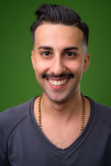 Young handsome Iranian man with mustache against green backgroun