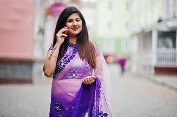 Indian hindu girl at traditional violet saree posed at street and speaking on phone.