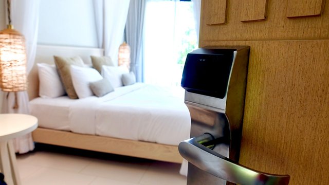 Close up of a card lock door handle in a luxury resort hotel and a wood panelled contemporary door, background of bed and pillows in the room