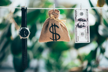 sackcloth bag, wristwatch and dollar banknote hanging on rope