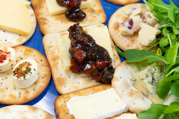 Crackers topped with a selection of cheeses, with sweet pickle and salad leaves. Close up view from above with focus on pickles. On a blue plate.