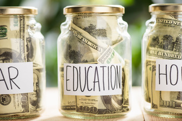 Glass jars with dollar banknotes and inscriptions car, education, house